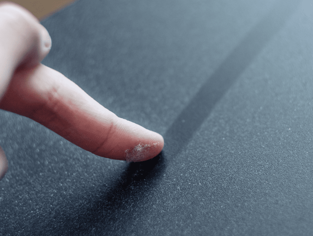 Finger eines Mannes, der eine Spur durch Staub auf einer dunklen Oberfläche zieht