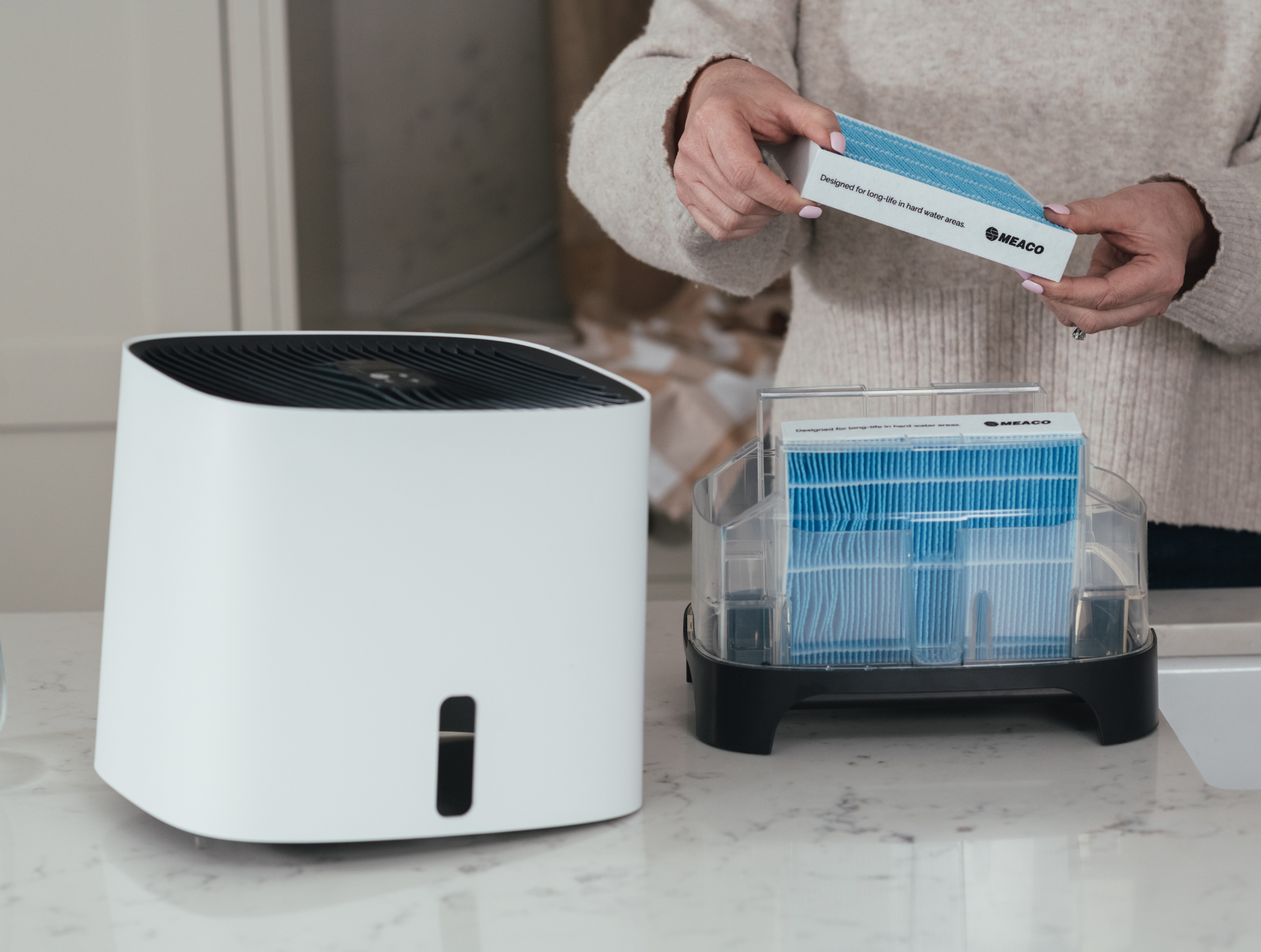 Die Hände einer Frau entfernen Armin-Luftbefeuchterfilter auf der Küchentheke.