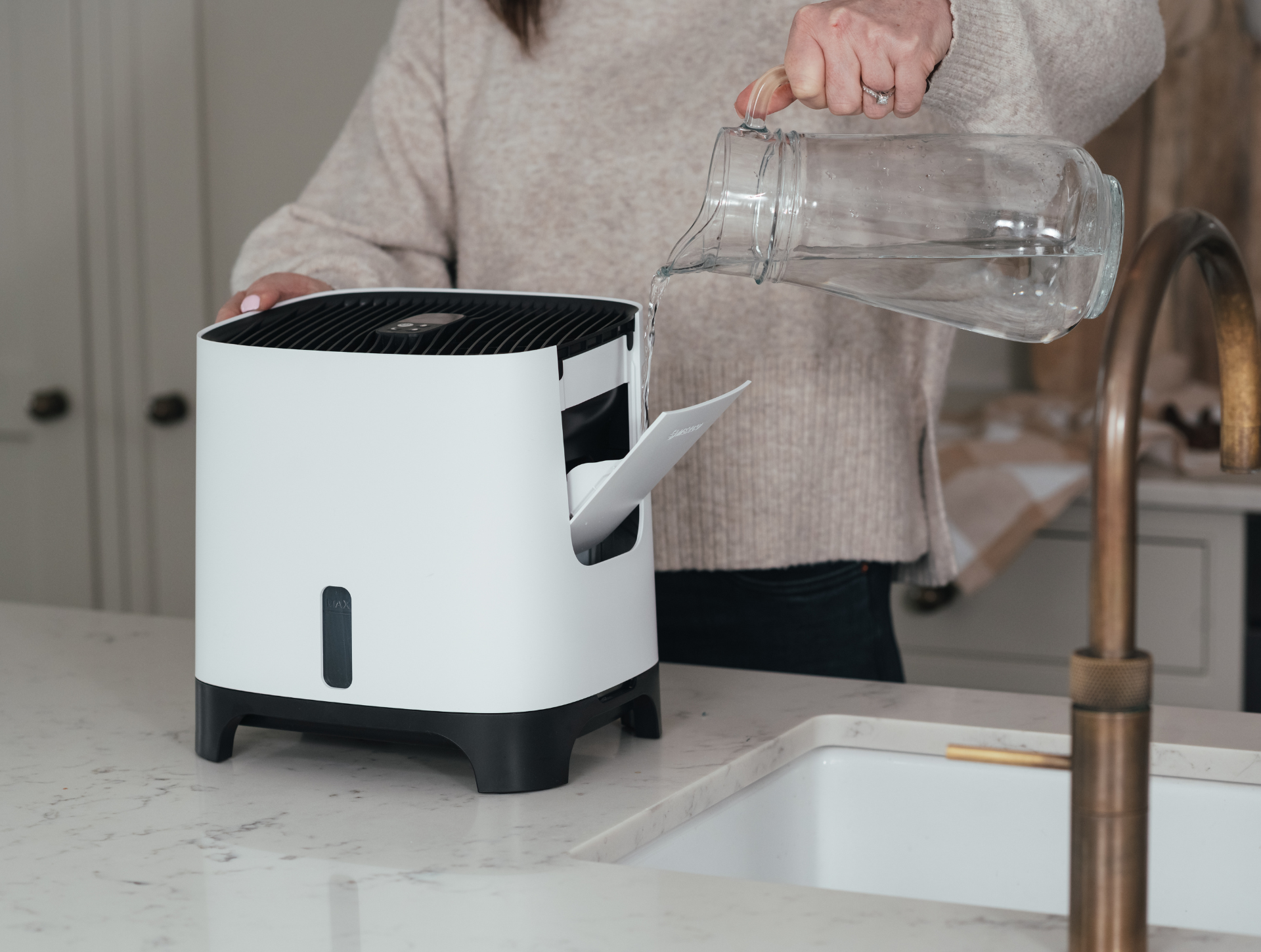 Frau, die Wasser aus einem Glaskrug in ihren Meaco Armin Luftbefeuchter gießt