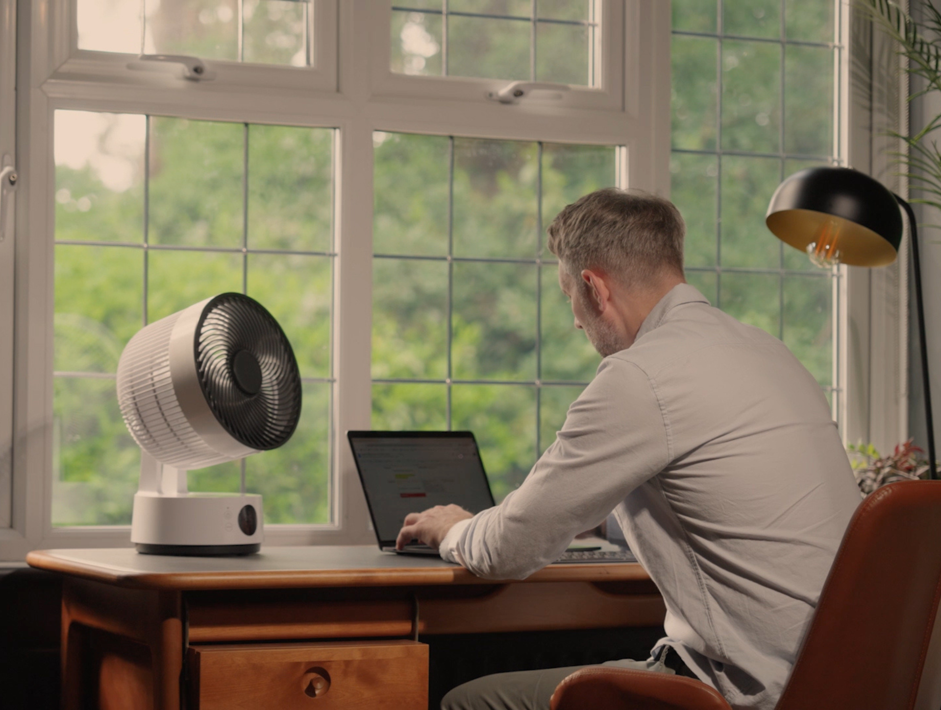 Ein Mann arbeitet zu Hause in seinem Arbeitszimmer, wobei ein Meaco-Ventilator für angenehme Kühle sorgt