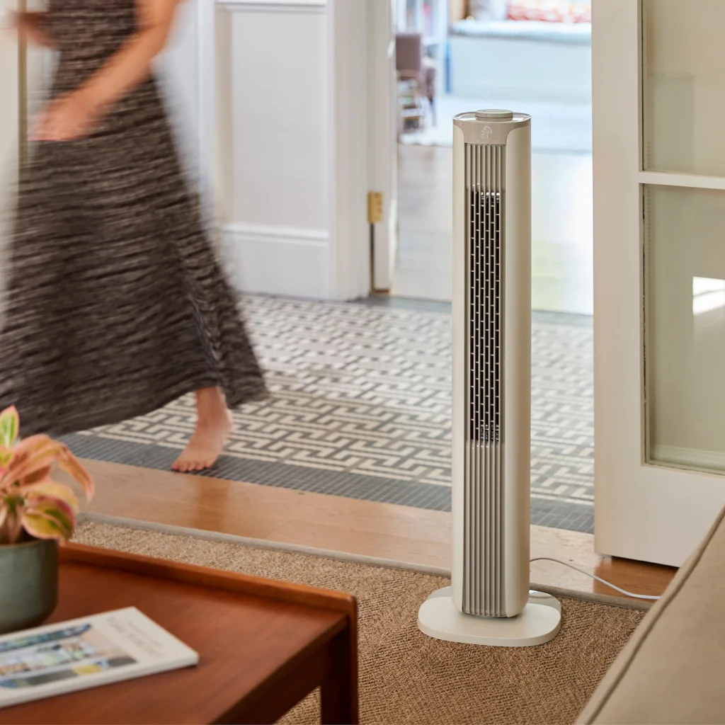 Der große Meaco Smart Turmventilator steht in einem Wohnzimmer. Neben ihm geht eine Person vorbei.