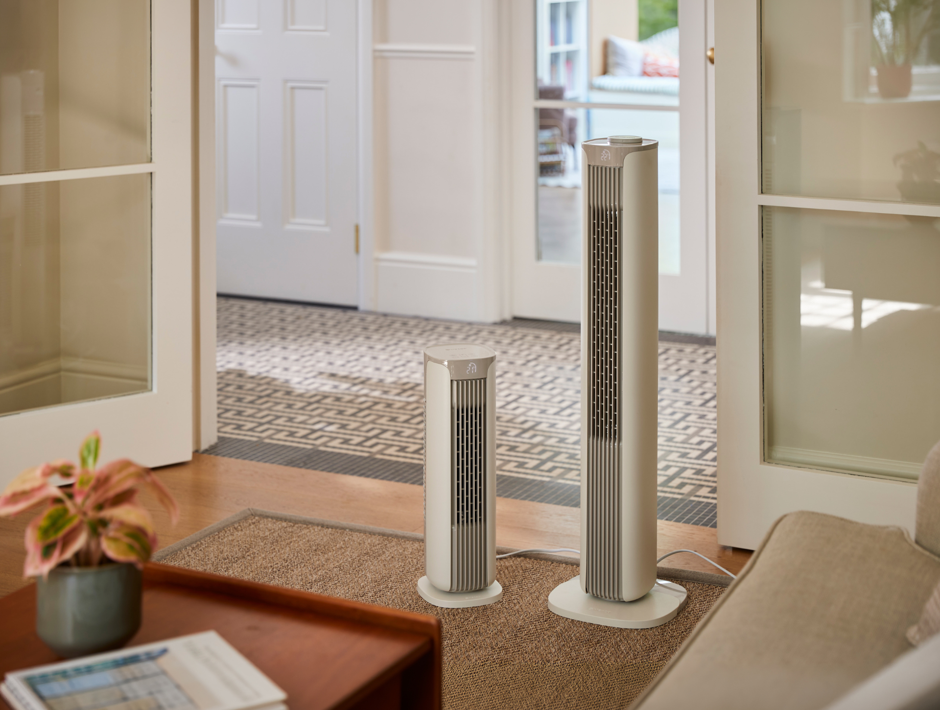 Die Meaco Sefte® Turmventilatoren in zwei Größen stehen nebeneinander im Eingang eines neutralen Wohnzimmers.