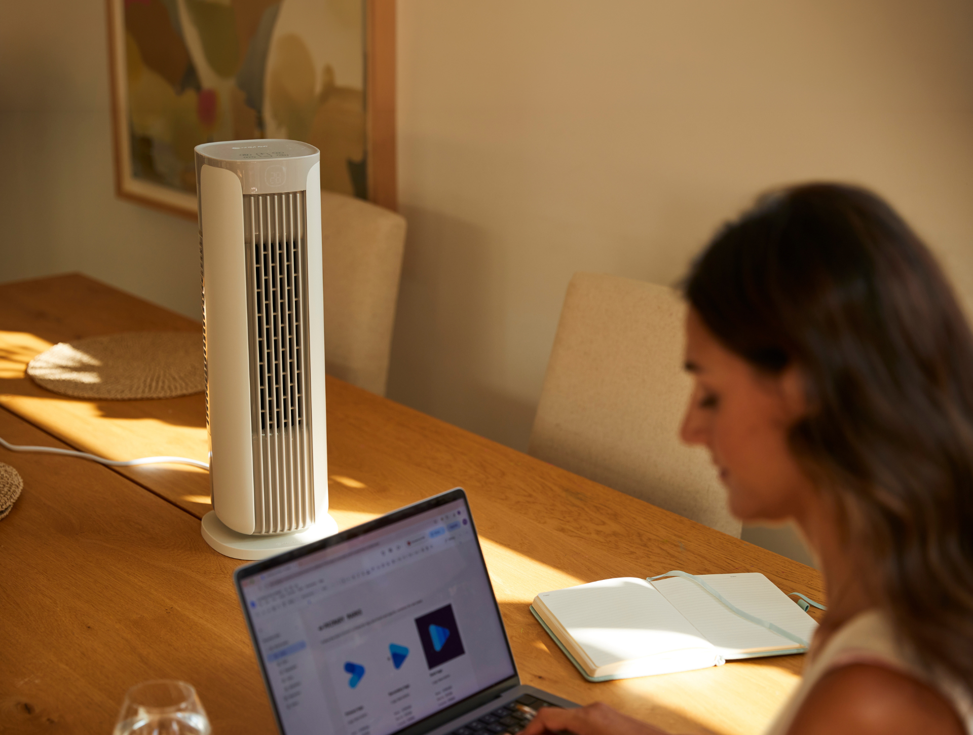 Une femme travaille sur son ordinateur portable à la table de la salle à manger, avec un petit ventilateur colonne Sefte® placé devant elle.